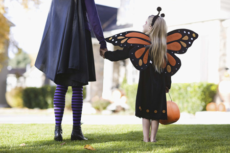 Young girl dressed in a butterfly costume holding her mom's hand