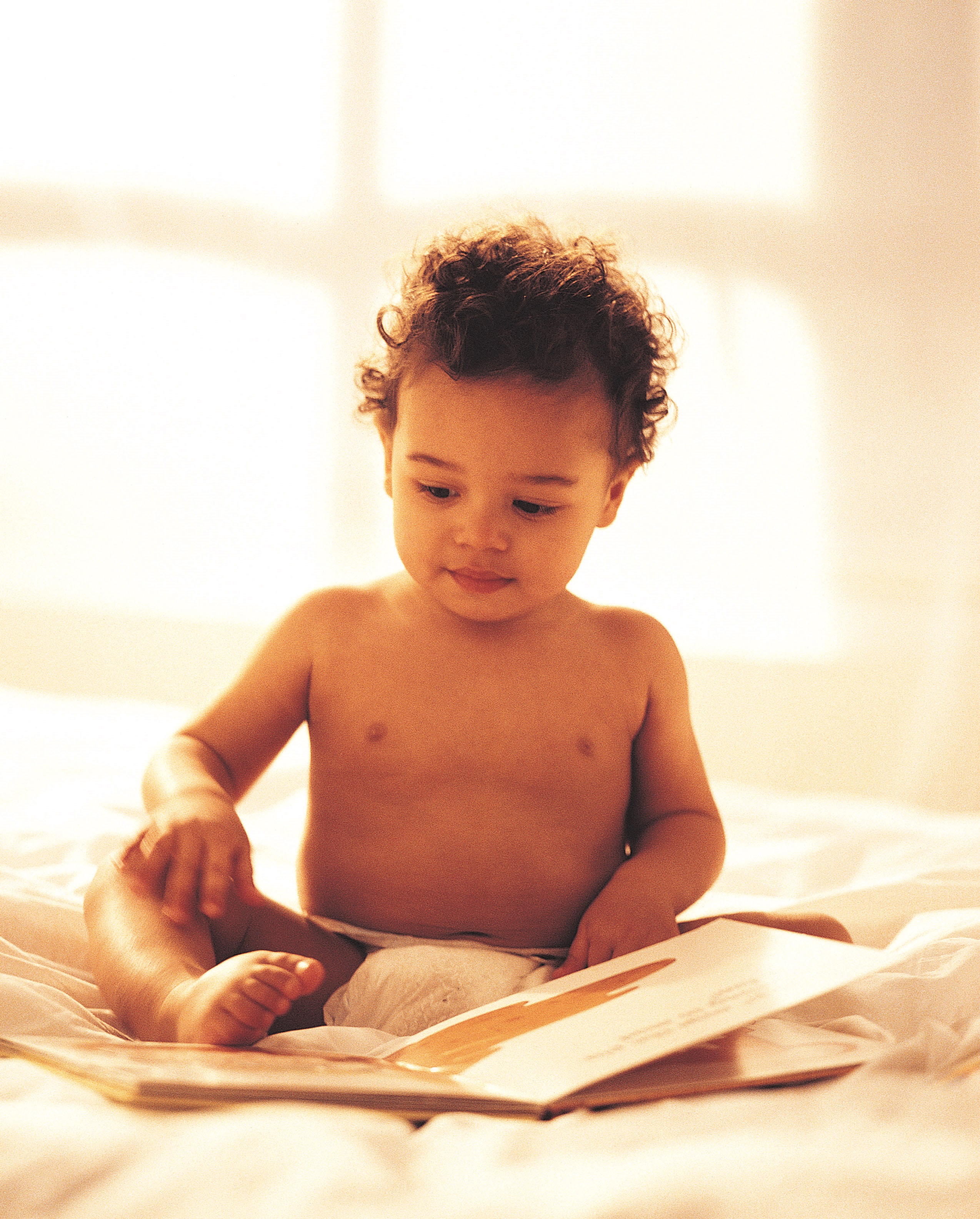 baby boy reading a book on a bed