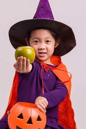 Small girl dressed as a witch holding an apple 
