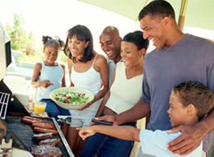 Family gathered around a barbeque grill, cooking burgers and hot dogs