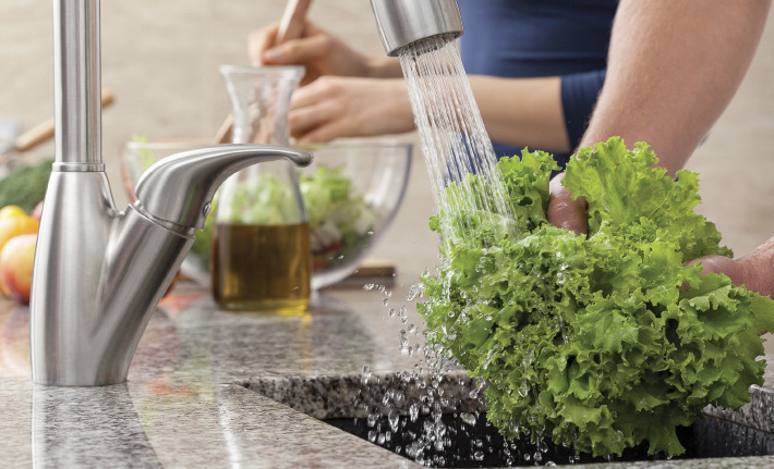 person washing lettuce in kitchen sink