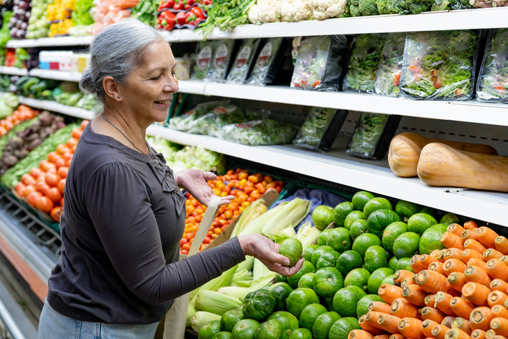 Older adult woman looking for vegetables in grocery store