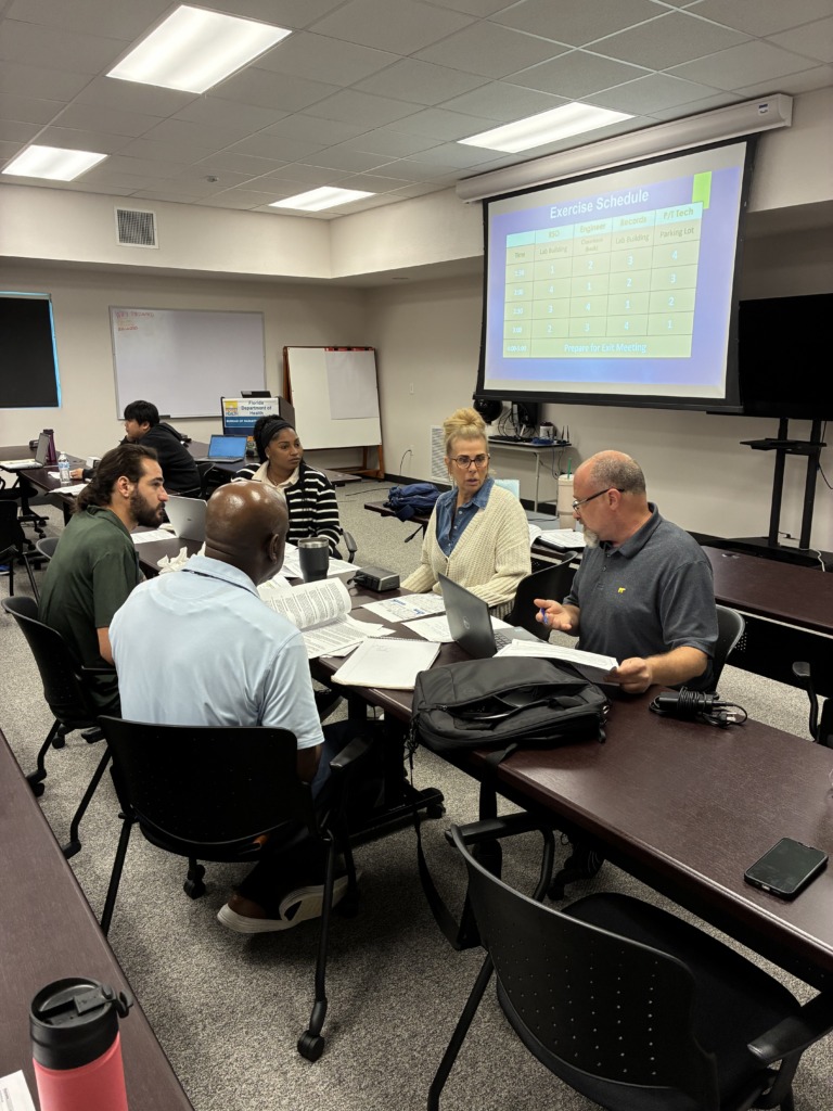 A group of people attending a meeting or training session, with an 'Exercise Schedule' projected on a screen and a 'Florida Department of Health' sign visible on the wall.