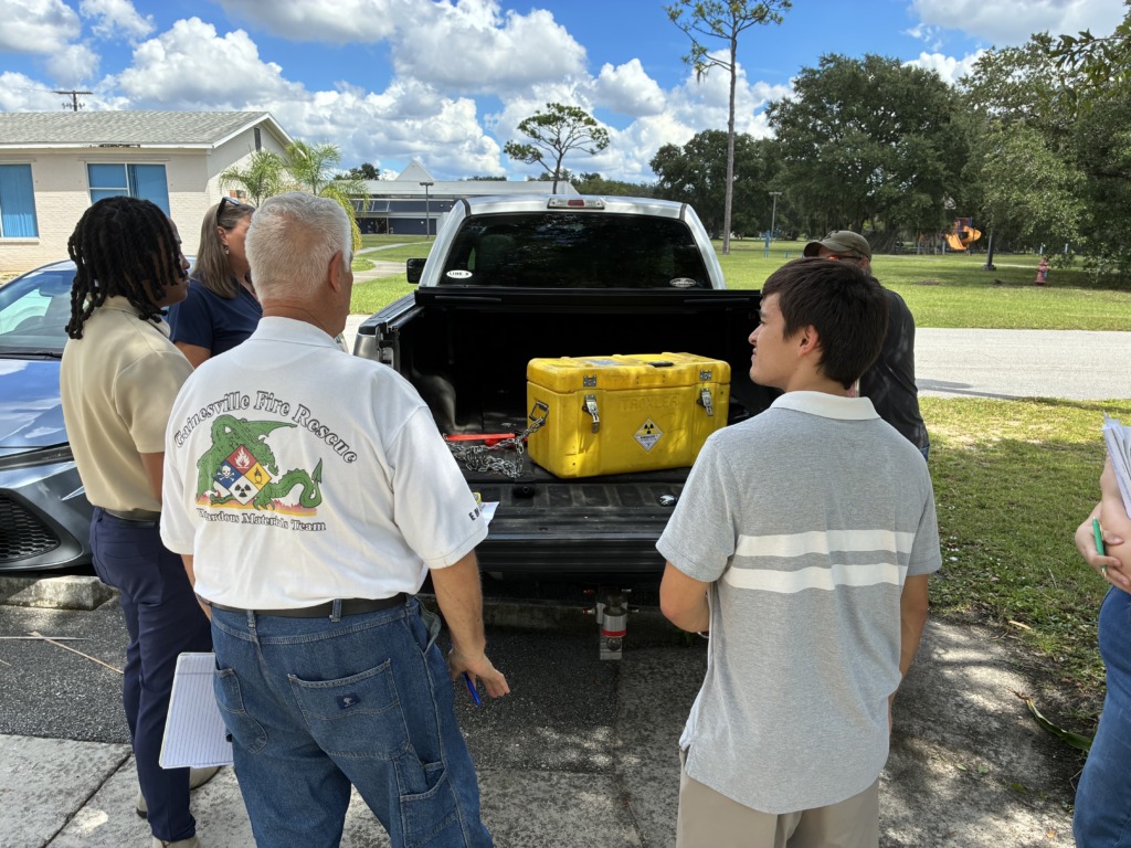 A group of five people, including members of the Gainesville Fire Rescue Hazmat Team, gathered around a pickup truck with a yellow Troxler radioactive case in its bed.