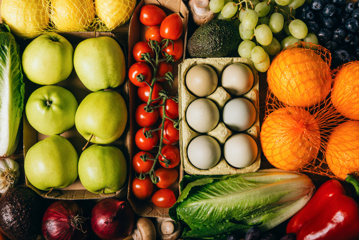 Overhead view of a colorful assortment of fresh fruits, vegetables, and a carton of six eggs