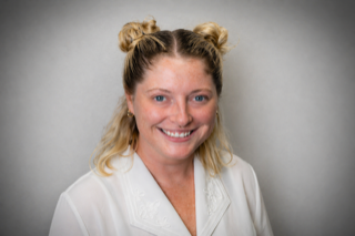 Headshot of a smiling woman with blonde hair in two top buns.