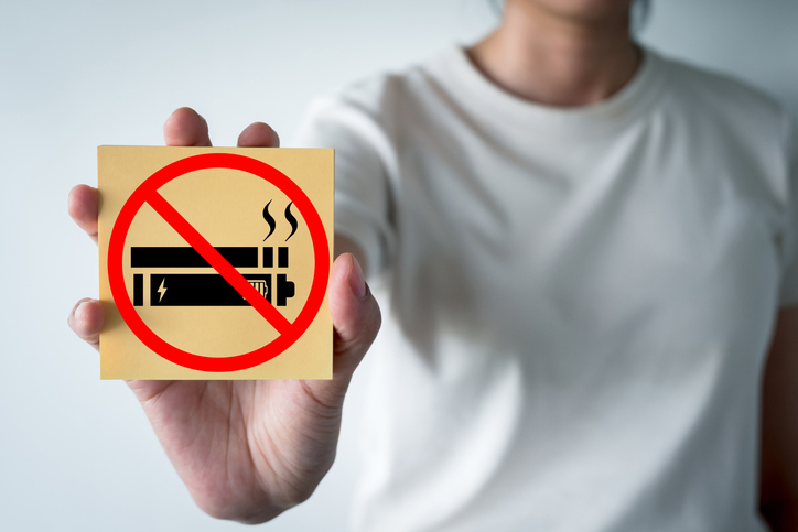 A hand holds a sticky note with a red 'no vaping or smoking' symbol